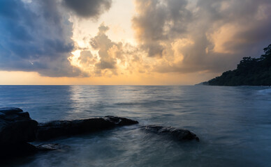 sunrise dramatic sky over sea horizon from rocky shore at dawn long exposure shot