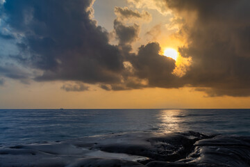 sunset dramatic sky over sea horizon from rocky shore at dawn long exposure shot