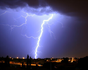 Naklejka premium Dramatic nighttime shot of a powerful lightning bolt striking over a suburban cityscape. The vivid flash illuminates the dark sky and houses below.