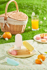 A spring picnic takes place on a green lawn, food and drink scattered arranged on a white picnic carpet with some unbranded sunscreen bottle displayed in center