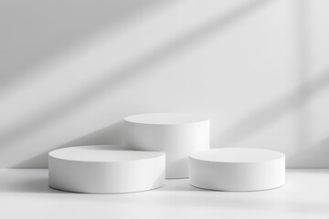 Three white cylindrical podiums on a white background with sunlight shadows.