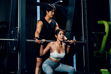 Obraz na płótnie Canvas Asian woman guy a squat exercise legs heavy weights with a barbell with the assistance of a trainer in gym interior, Man doing training lifting barbell to female at fitness gym center, sport workout