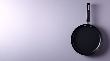 A black frying pan hanging against a simple background.
