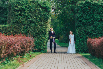 The bride and groom stand on a tree-lined path in a serene green park surrounded by tall trees.