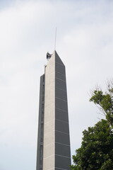 A tall minimalist tower with trees around it with a clear sky