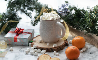 White cup of a hot chocolate with marshmallows on top, Christmas decorations and a Christmas tree, mandarins and cookies as a background. Warm Holidays season