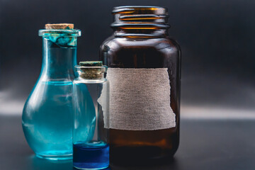 Assorted glass bottles with blue liquid and torn label on dark background