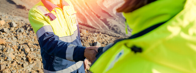 Construction industry workers shaking hands outdoors at open pit mining site in safety gear.