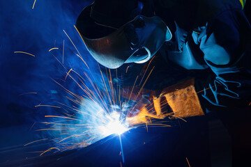 Factory industrial welder worker in workplace with spark, neon light. Professional welder fix industry truck