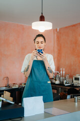 Young female entrepreneur hanging a welcome sign in front of a coffee shop. Beautiful waitress or...