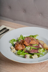 Baked piece of meat among green salad and vegetables on table in restaurant