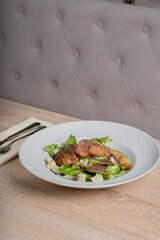 Baked piece of meat among green salad and vegetables on table in restaurant
