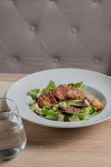 Baked piece of meat among green salad and vegetables on table in restaurant