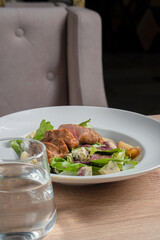 Baked piece of meat among green salad and vegetables on table in restaurant