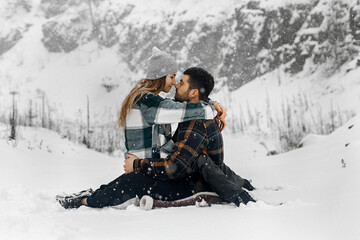 couple sitting on the snow in a winter landscape. A man and a woman hug and look at each other with tenderness.