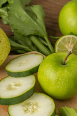 Close-up of green apples, cucumber slices, celery, and lime on a wooden surface, ideal for healthy recipes or detox drinks.