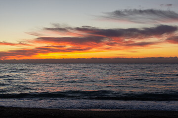 Orange sunset on the sea. Bright juicy landscape with feathery clouds on the horizon. Purple, lilac, pink shades of the evening sky. The smooth surface of the sea, a boat sails by. Idyll, relaxation
