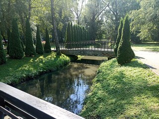a stone bridge crossing a small river, surrounded by green trees and lush bushes