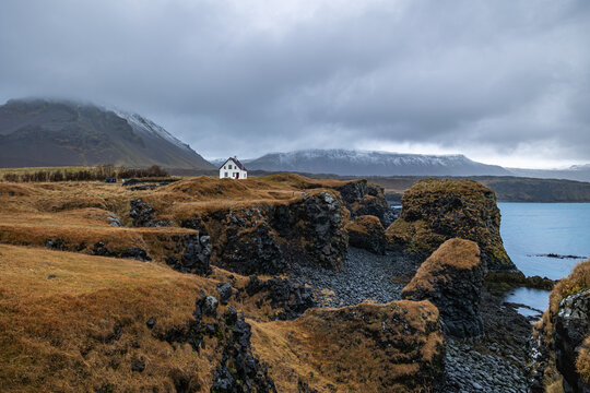 Arnarstapi coast with bizzar rock formation and a lonely little white house, the Snaefellsnes mountain stands at the background