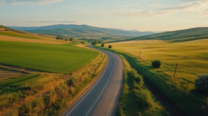 Scenic winding road through hilly rural landscape with vibrant green fields and distant mountains under a clear blue sky