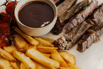 Delicious grilled steak served with crispy fries and roasted tomatoes on a white plate