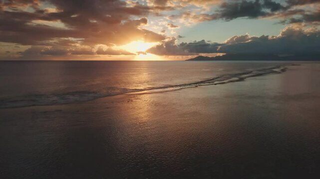 Golden hour sunset reflects on gentle ocean waves washing shallow reef, mountain coastline of Tahiti island in French Polynesia, picturesque tropical seascape under bright colorful sky. Aerial view