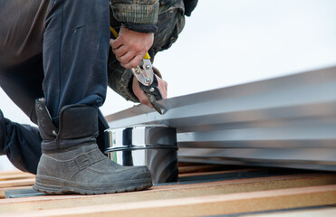 A man is working on a roof, using a pair of pliers to cut a piece of metal