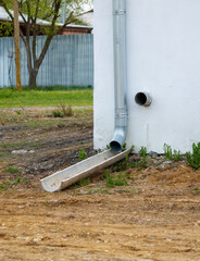 A pipe is attached to a building and is surrounded by dirt