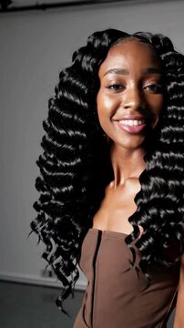 A stunning female model in minimalist studio. Her black hair is wig extremely long hair that goes under her hips with small zigzag-shaped curls or coils that are densely packed together 