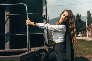 a girl stands next to a railway carriage and holds on to a metal ladder attached to the carriage....