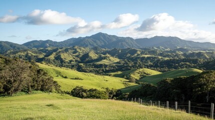 Obraz premium Rolling green hills and mountains under a blue sky with fluffy clouds.