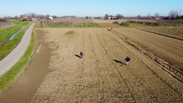 a pair of treasure hunters with metal detectors in a plowed field ready for cultivation

