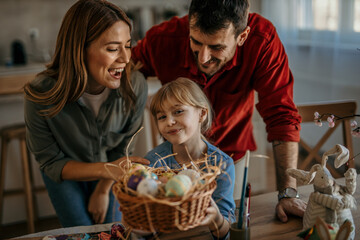 Parents and children smiling while decorating eggs with vibrant paints and glitter for Easter.