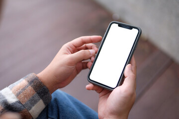 A man holds a mobile phone with a blank face while sitting in a park.