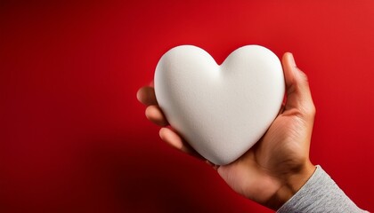 hand holds a white, heart-shaped foam object against a red background.