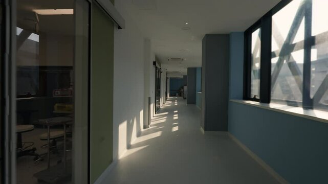 Sunlit corridor of a modern hospital with large windows and reflective surfaces creating patterns of light on the floor. Concept of contemporary healthcare architecture and serene medical facilities