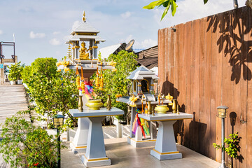 Chonburi, Thailand - November, 18, 2024: Traditional Thai Spirit House with Golden Statues and Colorful Garlands at Chonburi, Thailand.