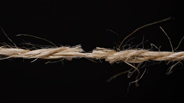 jute or hemp rope Side view of a frayed rope with fibers unraveling, emphasizing the breaking tension under strain against a dark background.