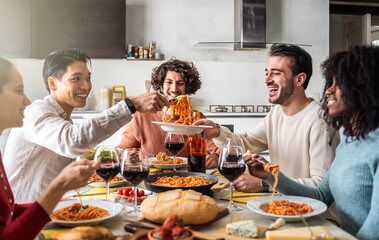 Group of smiling friends sharing spaghetti and wine at a kitchen table. Diverse young adults enjoying a warm meal together, celebrating friendship and connection in a modern and inviting space.