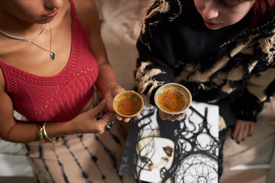 Unrecognizable girls sitting on bed, holding old-fashioned piyalas with green tea, from above view