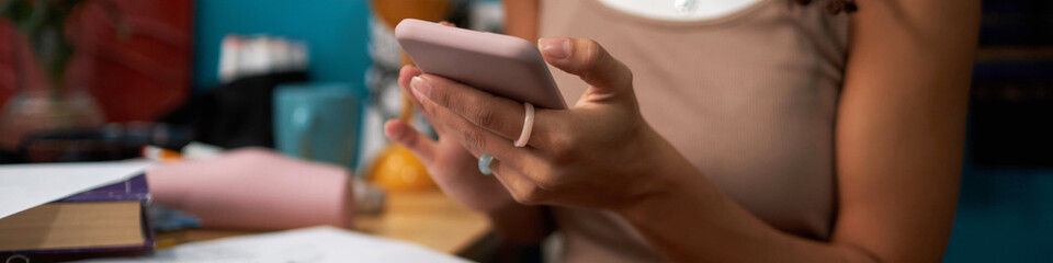Obraz premium Medium section of biracial girl using smartphone while sitting at desk and studying in her dorm room, website header