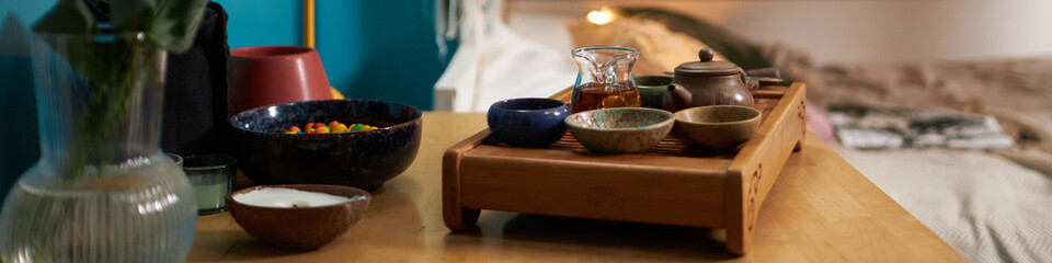 Traditional tea set on wooden table in cluttered dorm room interior, copy space, website header