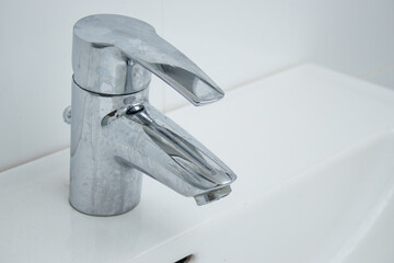 Close up of a bathroom faucet with limescale stains and dirty sink