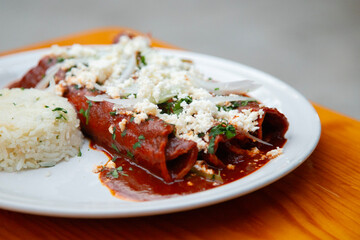 Traditional enchiladas with Oaxaca cheese, red mole and rice. Enchiladas are a dish from Mexican cuisine made with rolled or folded corn tortillas.