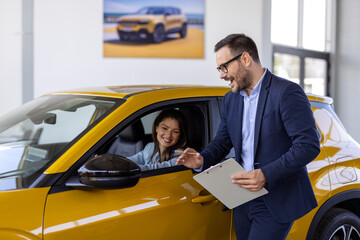 Car Sales Manager Showing Auto To Caucasian Lady Buyer Standing In Luxury Automobile Dealership Store. Buying Vehicle Concept