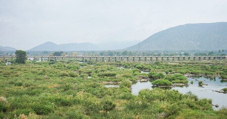 India, Karnataka, a large green field with Satthegala bridge and mountain in the background