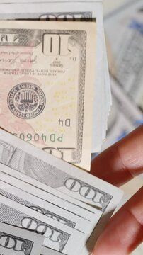Vertical video. From a large stack of hundred-dollar bills, only a single ten-dollar note is handed over, highlighting value disparity or minimal reward.