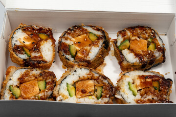 A box of sushi with six rolls inside. The rolls are filled with meat, vegetables, and rice