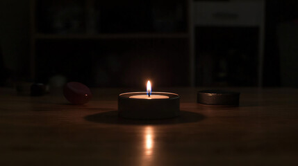 Dark room with single candle flickering on wooden table during power outage, creating serene atmosphere with soft glow illuminating scattered items.