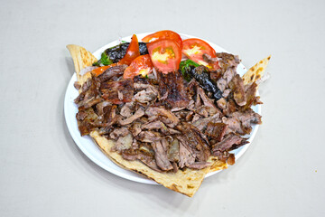 Turkish  Traditional Ramadan doner kebab with tasty tomato sauce and rice or turkish pilav in white plate on table background. Lavash doner kebab ( doner zurna durum )  Pilavustu Doner Iskender kebap
